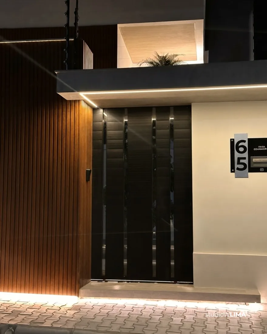 Acesso da Casa Comemorar com portão em ripado de madeira escura, número da casa e iluminação de LED no piso