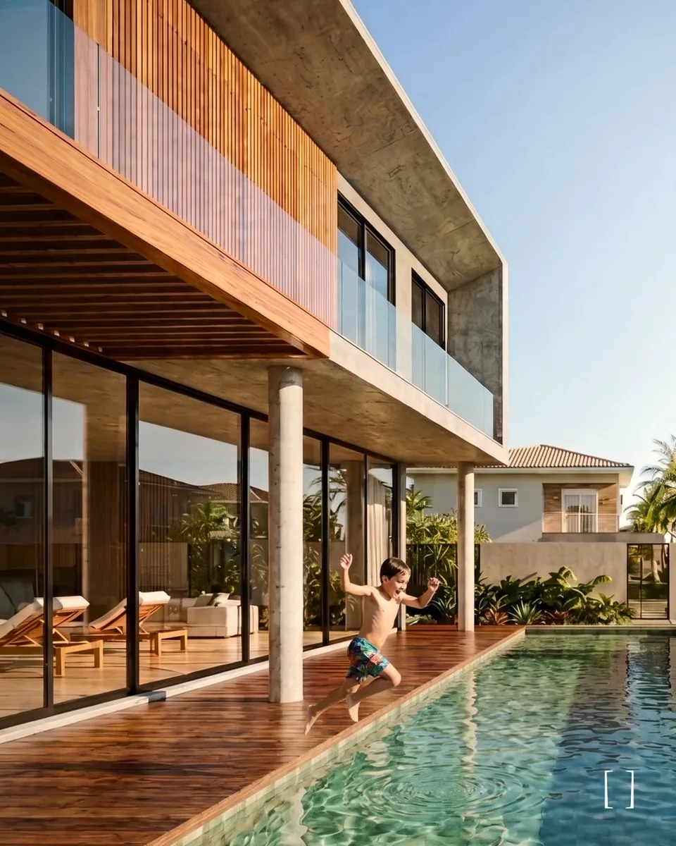 Deck de madeira e piscina da Casa Itapema, com pilares de concreto, grandes planos de vidro e varanda de vidro no pavimento superior